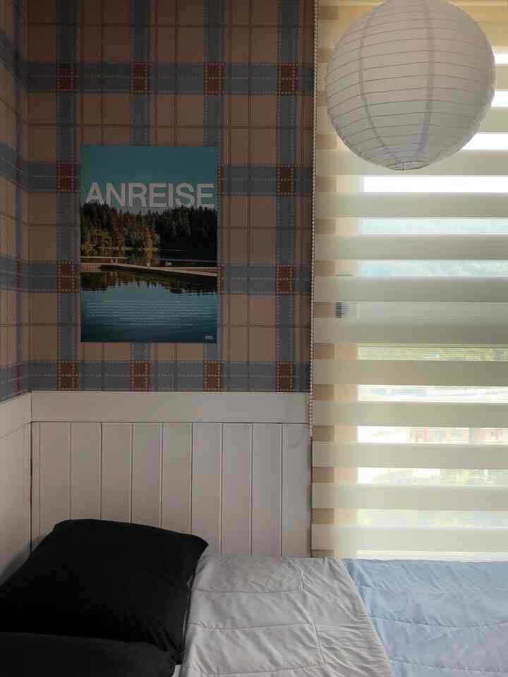 ナチュラルカラーの寝室、枕と寝具があるベッド、ベージュのブラインドと風景のポスターが配置された落ち着いた空間