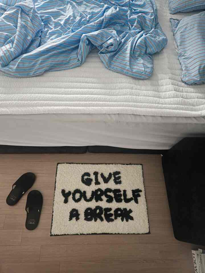 A white and blue toned bedroom featuring a black lettering mini rug and black slippers with a simple interior style