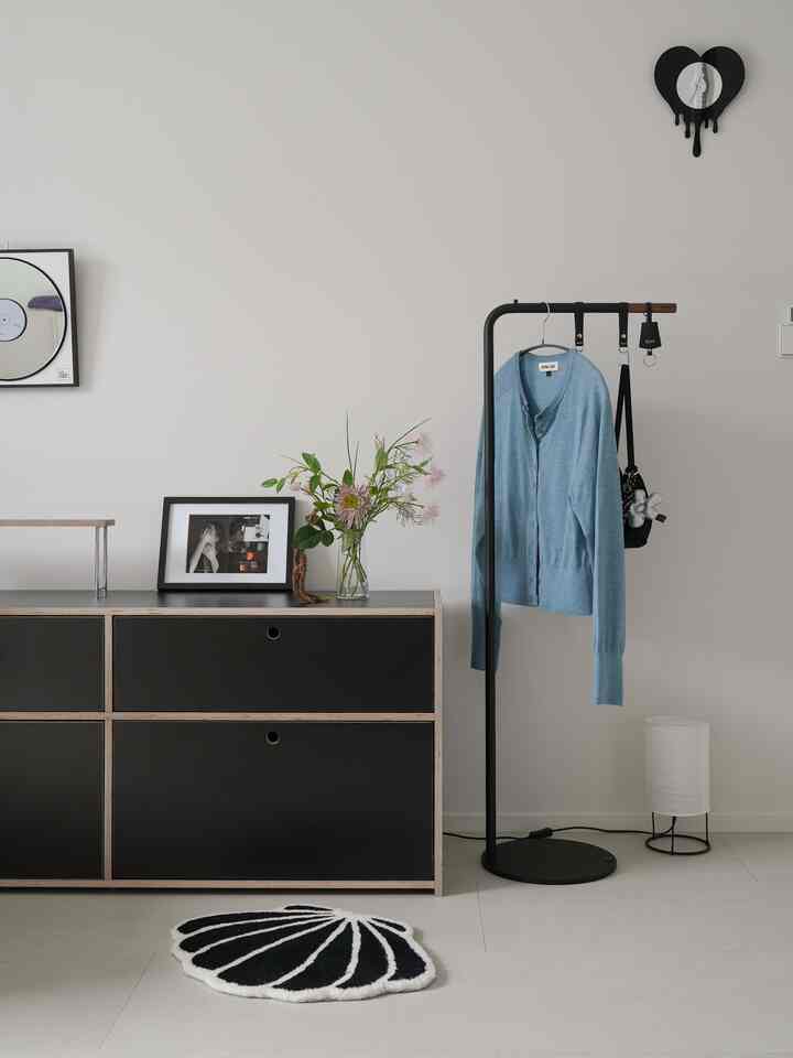 ミニマルでモダンな黒と木目調の寝室、黒のハンガーとドレッサーが小物とラグに囲まれた落ち着いた雰囲気のインテリア