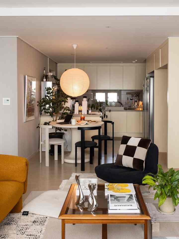 ナチュラルカラーのモダンなダイニングとキッチン、丸いダイニングテーブルと黒い椅子、オレンジのソファとアームチェアが配置された温かみのある空間