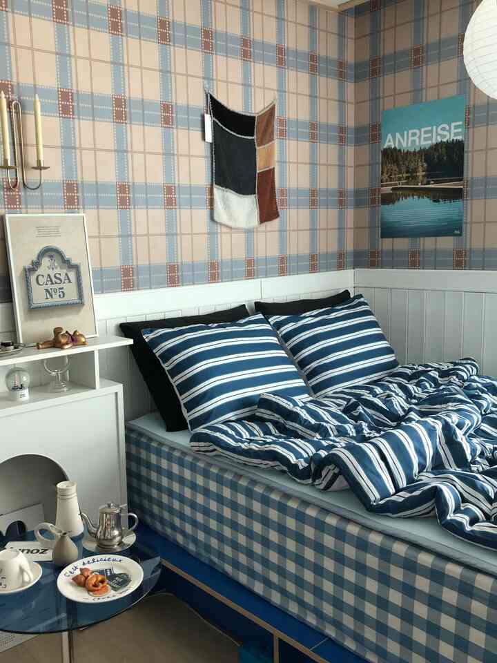 A blue and beige toned bedroom featuring a check-pattern bed frame and striped bedding in a cozy setting