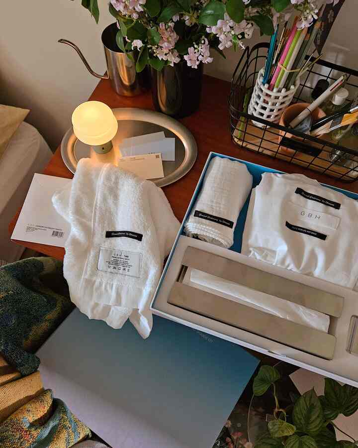 白と木目調の寝室のテーブルに、タオル、テーブルランプ、花瓶が配置された雰囲気のある空間
