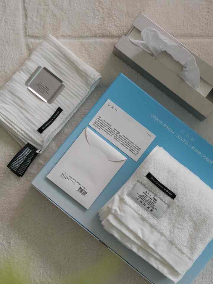 アイボリーとホワイト調のバスルーム用タオル、ステンレストレイ、ティッシュケースが配置されたナチュラルな雰囲気のインテリア