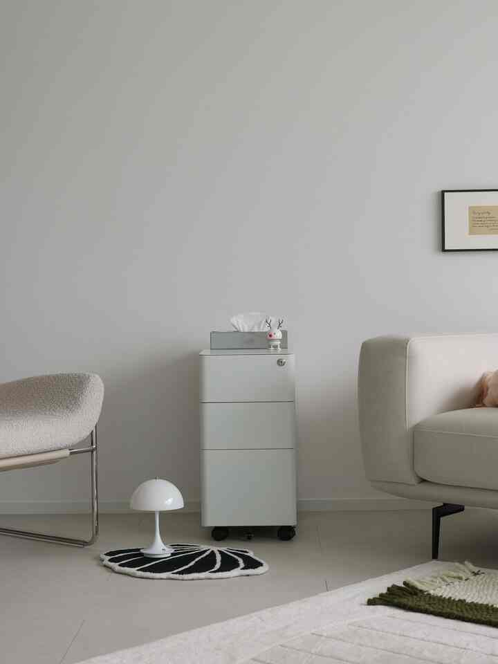 ナチュラルトーンのシンプルなリビングルーム、ベージュのソファとアームチェア、サイドキャビネット、小さなテーブルランプが配置された落ち着いた空間