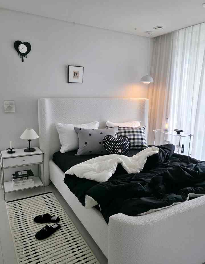 白と黒のモダンな寝室、ふかふかのベッドにブラック＆ホワイトの掛け布団とパターン入りの枕が配置された清潔感あるインテリア