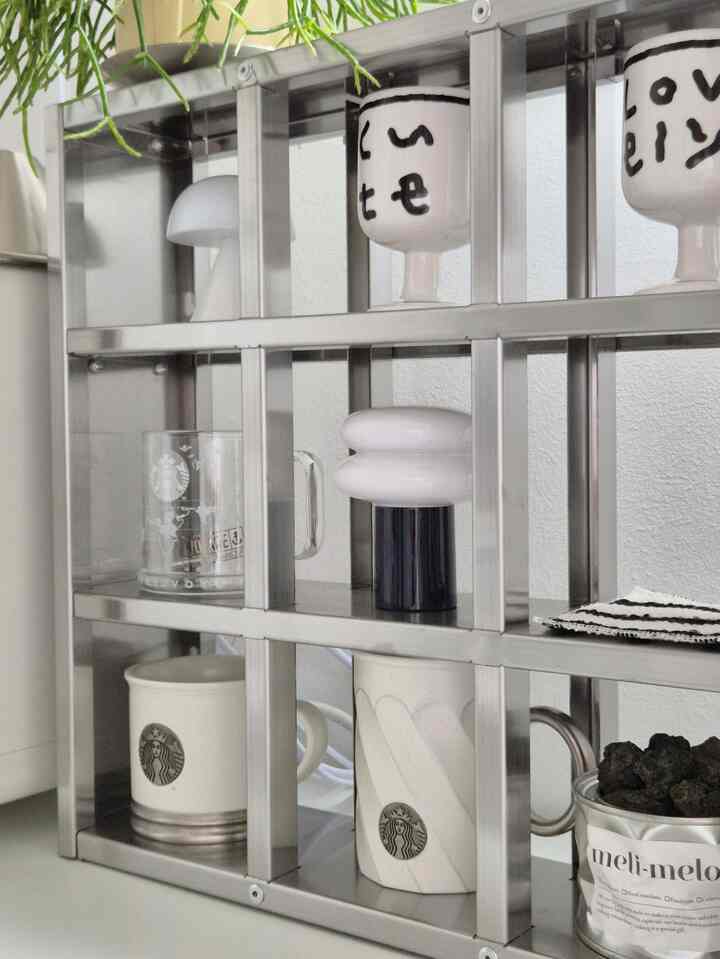 Modern kitchen shelf in white and gray tones featuring plants, a table lamp, diffuser, and coffee mugs neatly arranged