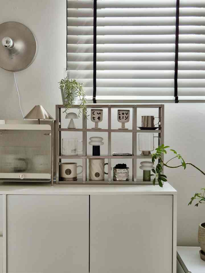 White and silver toned storage area featuring a metal rack with mugs and plants in a minimal and modern interior
