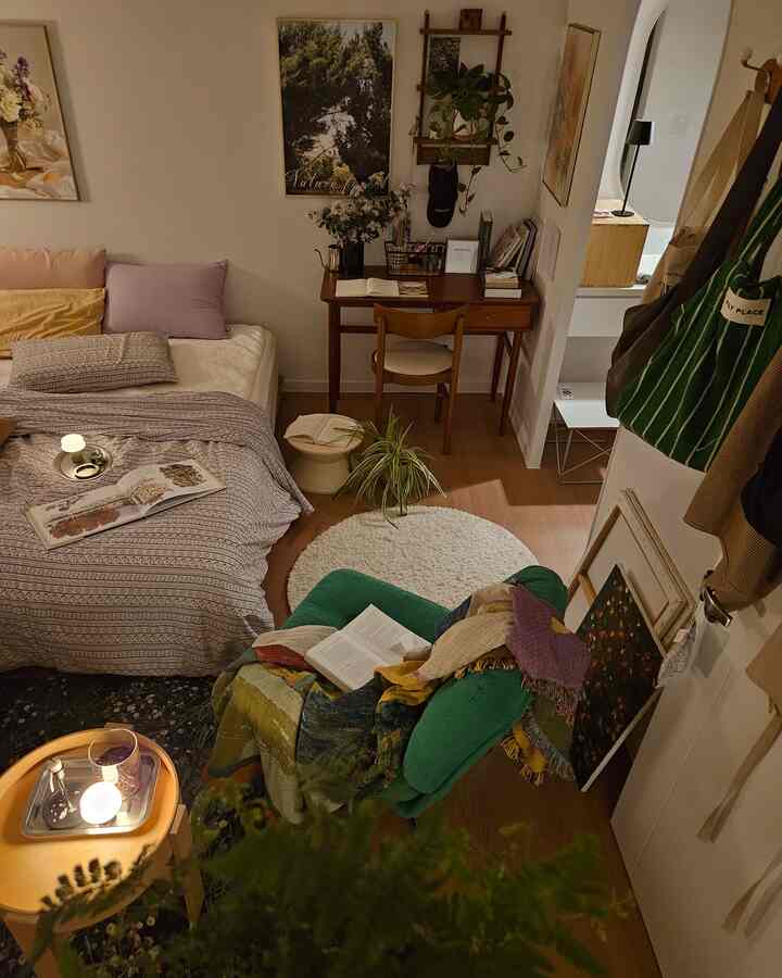 ナチュラルな木目調と白を基調としたコンパクトなワンルーム寝室で、デスクや植物が配置された落ち着いた作業空間
