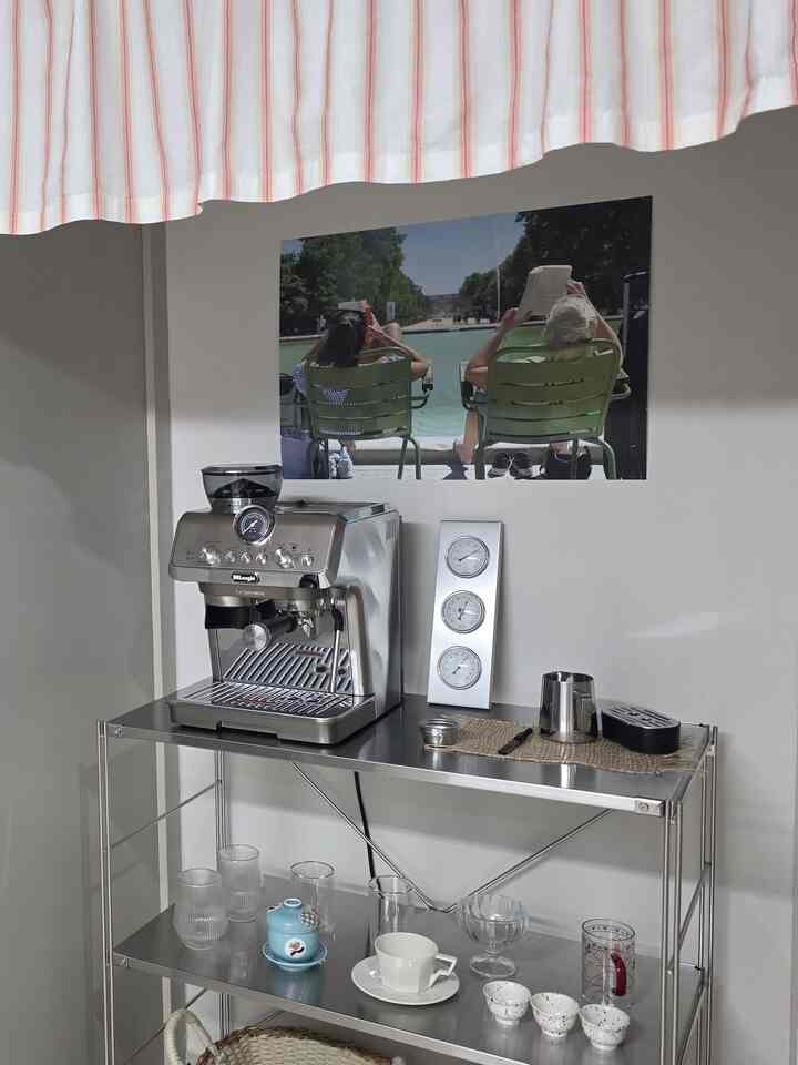 シルバー調のキッチンスペース、ステンレス棚とデロンギのコーヒーマシン、雰囲気のあるポスターが配置された清潔なおうちカフェエリア