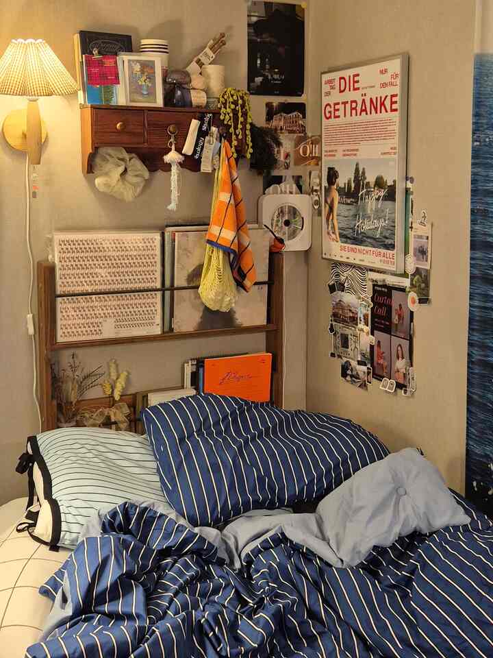 ネイビーの寝具がある居心地の良い寝室、壁掛け照明と多様な額縁やポスターが配置された空間