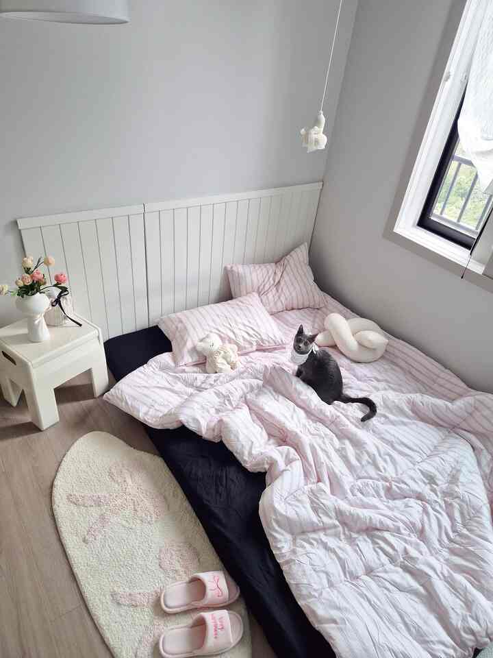 Cozy bedroom in white and pink tones, featuring a cat sitting on the bed