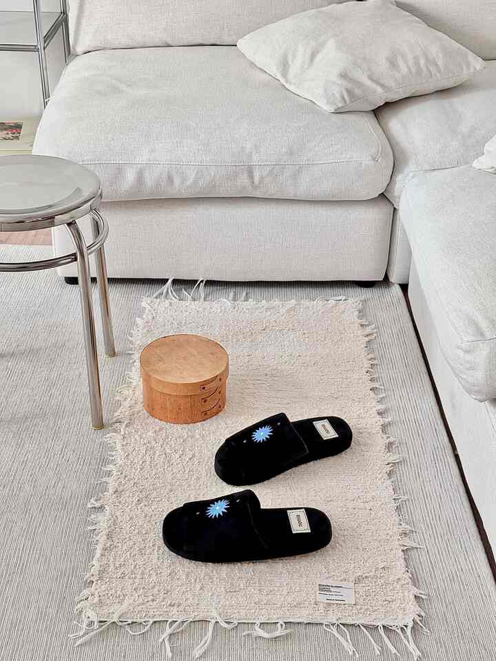 白とベージュを基調としたリビング、シンプルなデザインの4人用ファブリックソファとベージュのラグ、黒いスリッパが置かれた雰囲気のある空間