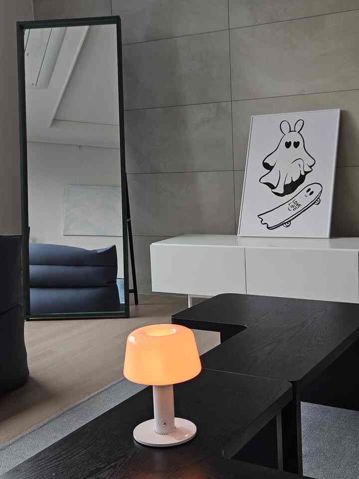 白と黒のモダンなリビング、オレンジ色の小さなテーブルランプと大きな姿見が配された印象的な空間