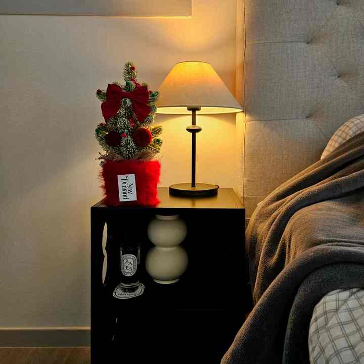 ベージュ色調の寝室、ナイトテーブルの上にテーブルランプとクリスマス飾りが置かれた雰囲気あるインテリア