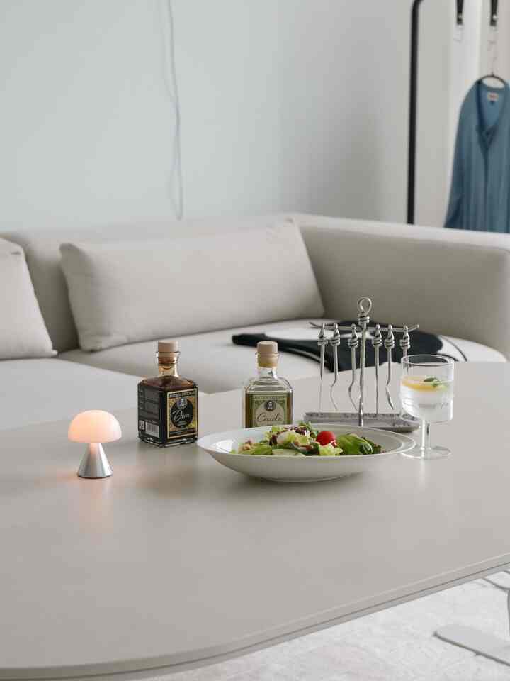 白とライトグレーのトーンのリビングルーム、シンプルなソファとミニカトラリーセット、ムードテーブルランプが配置されたモダンな空間