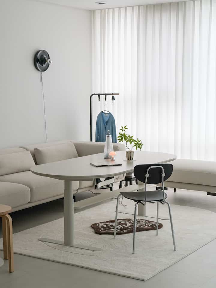 ホワイトとベージュのトーンのリビング、丸みのあるモーションテーブルと大型ベージュソファが配置されたモダンな空間