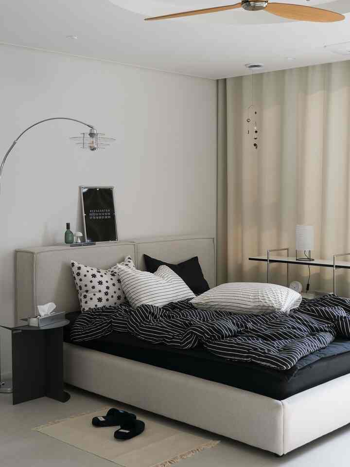 ベージュとモノトーンが調和した寝室、ストライプの黒い寝具とシンプルな家具が配された落ち着いた空間