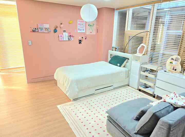 ピンクの壁と白いベッド、木目調のブラインドが配置された中学生の娘の居心地の良い寝室