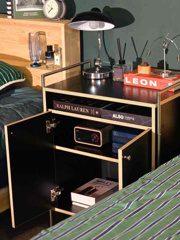 Cozy bedroom with green bedding and wood tone headboard featuring a black nightstand with a table lamp