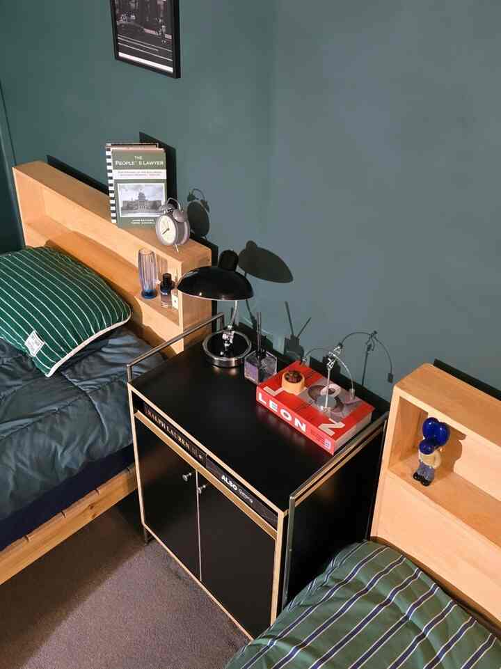 Modern bedroom featuring natural wood bed frames with green bedding, neatly arranged black nightstand and table lamp