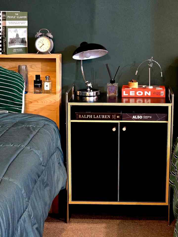 Classic style bedroom with deep green walls and black dresser, featuring vintage alarm clock and table lamp in a cozy setting
