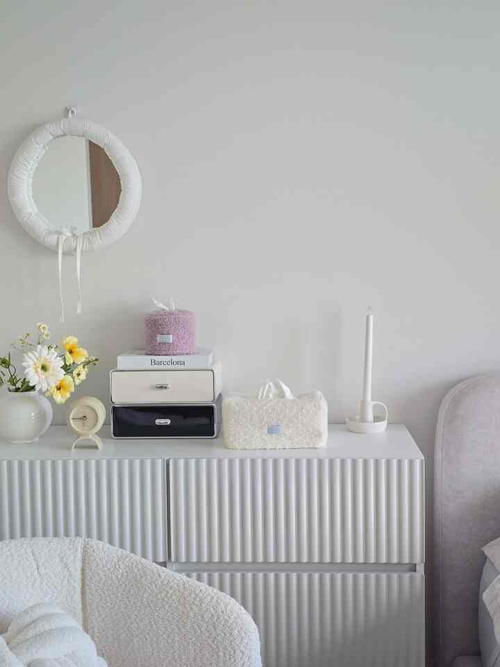 柔らかなホワイトトーンの寝室ナイトテーブルにブークレティッシュケースと丸い鏡、花瓶が配置されたナチュラルでミニマルなインテリア