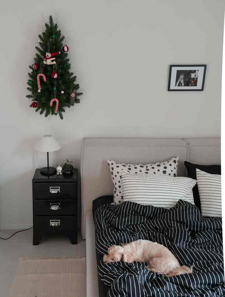 グレー調の寝室、黒のナイトテーブルと装飾されたクリスマスツリーが配置された落ち着いた空間