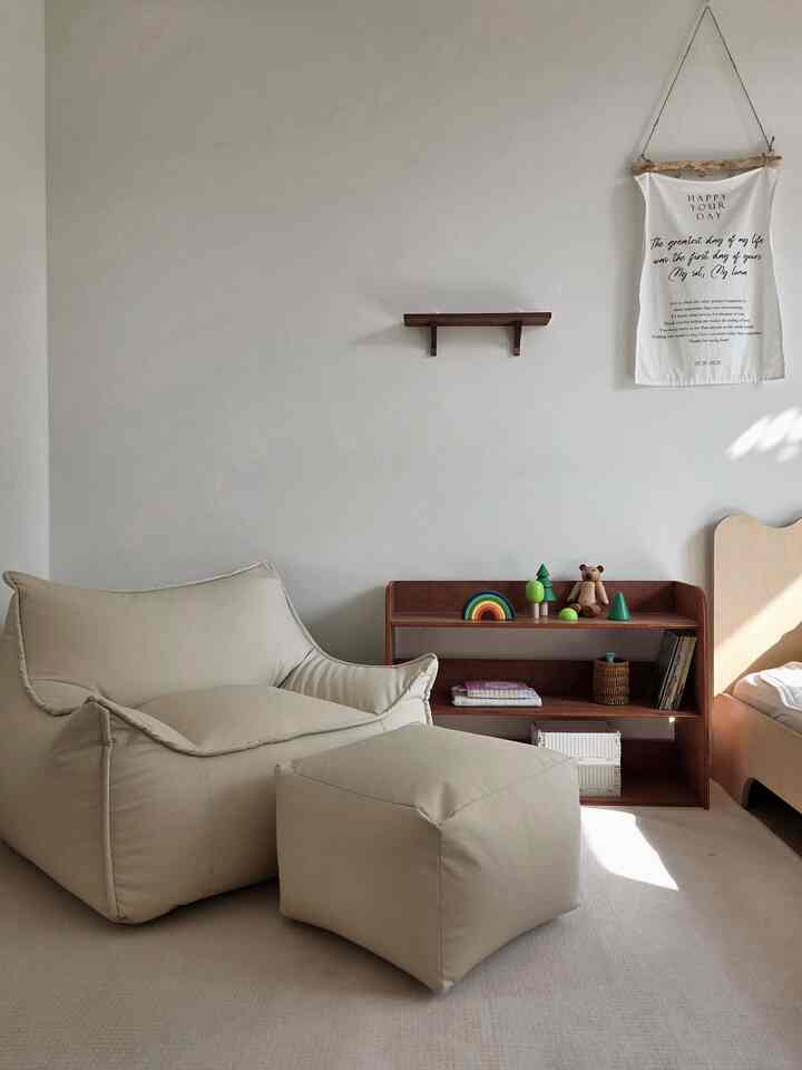 ベージュトーンのビーズクッションと木製の本棚が置かれた子供部屋、暖かく快適な雰囲気のあるインテリア