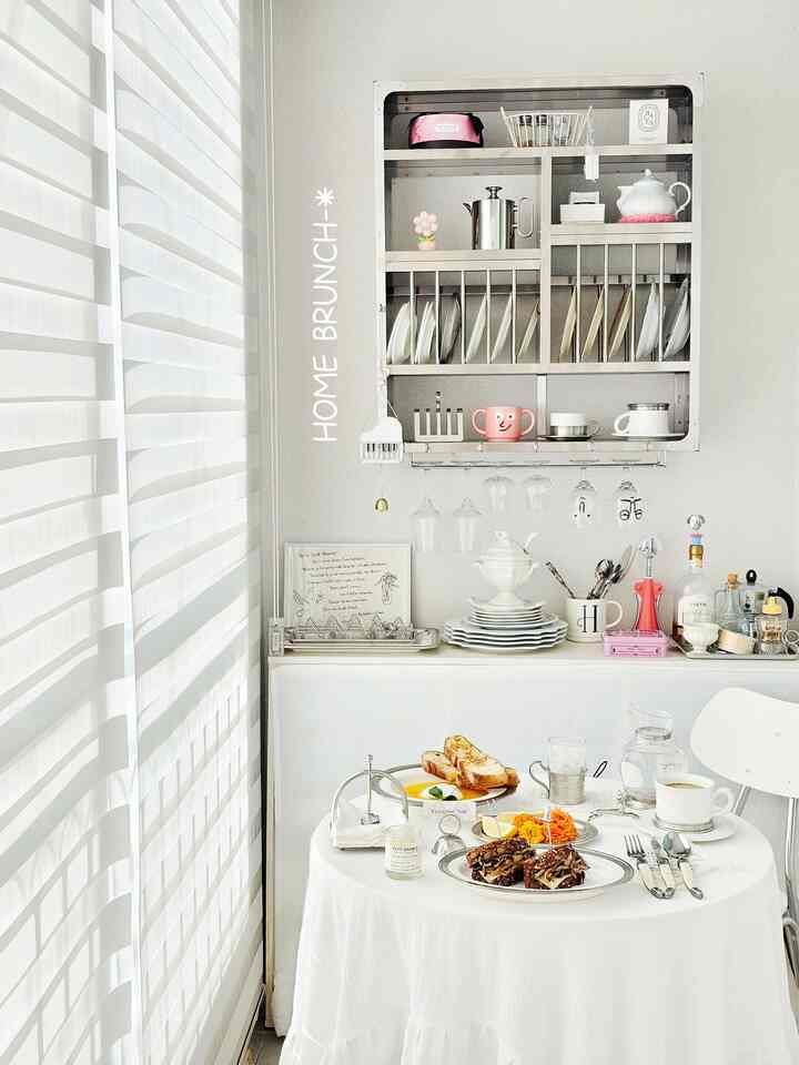 明るいホワイトトーンのダイニングルーム、丸いダイニングテーブルと壁掛けキッチンラックが配置された清潔で居心地の良いおうちカフェ空間