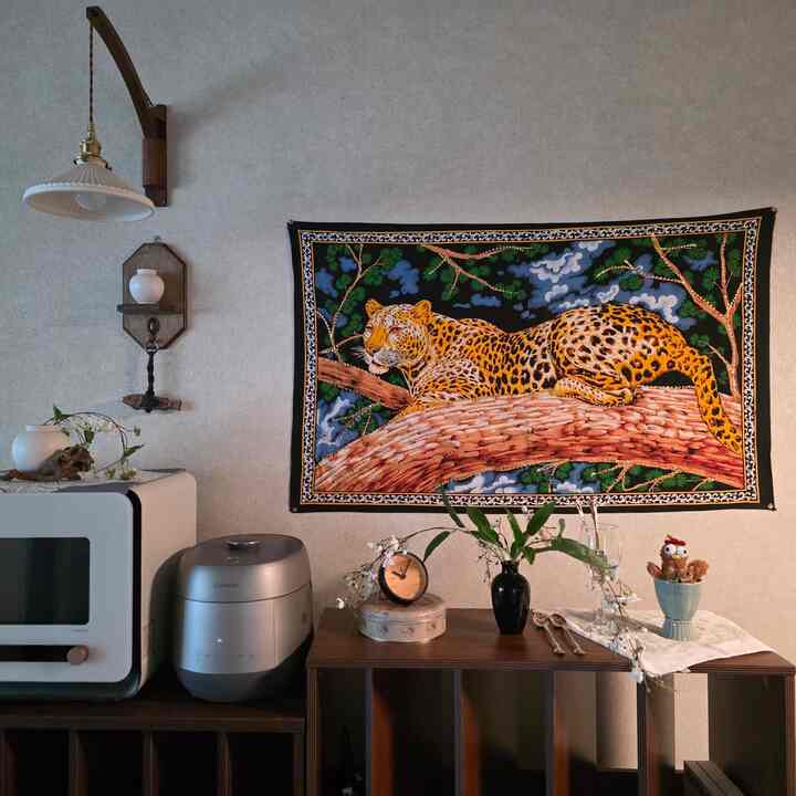 グレーの壁にヴィンテージのチータータペストリーが掛けられたキッチンスペース、木製家具とインテリア小物が配置された雰囲気のある空間