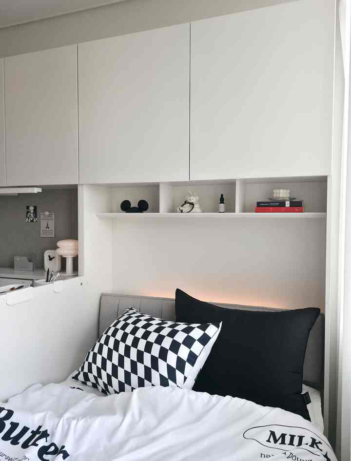 白と黒のトーンのミニマルな寝室、収納キャビネットとベッド、チェック柄クッションが配置された空間