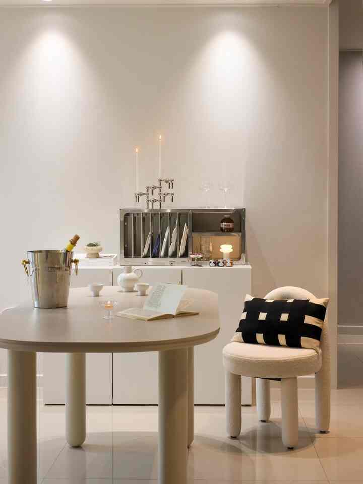 White-toned dining room featuring a modern dining table and chair, plate rack, and storage cabinet in an elegant setting
