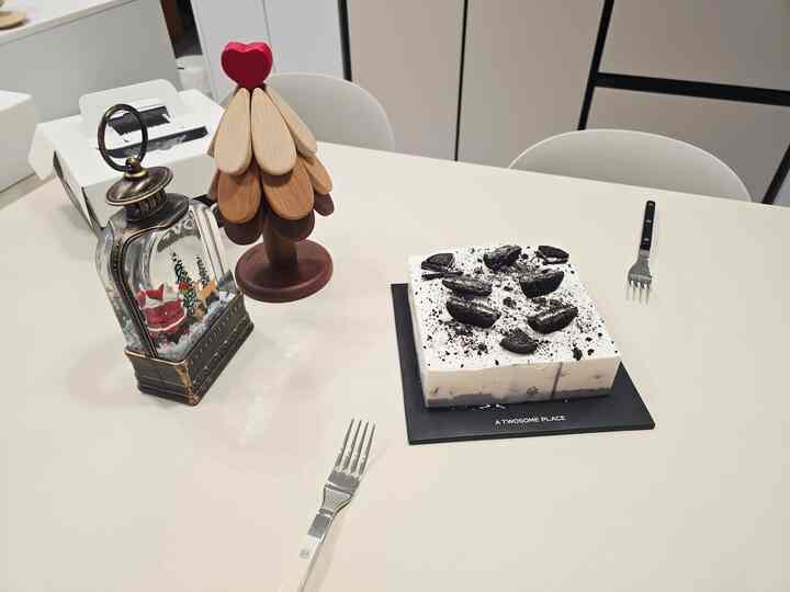 ホワイト色調のダイニング、ダイニングテーブルとチェア、ナチュラルな木製オブジェとクッキーが乗ったケーキが配置された清潔で温かみのある空間