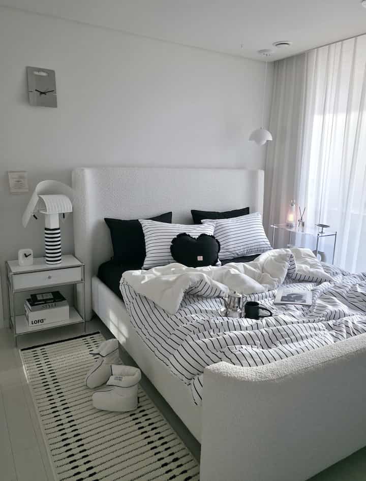 白と黒のストライプ寝具セットが配置されたモダンな寝室、大きなファブリックベッドとペンダントライトが印象的な明るくすっきりした空間