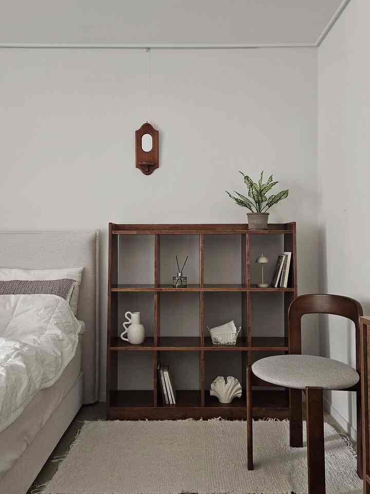 ホワイトの壁とベッド、ウォールナットの本棚と木製スツールが配置されたナチュラルな雰囲気のある寝室