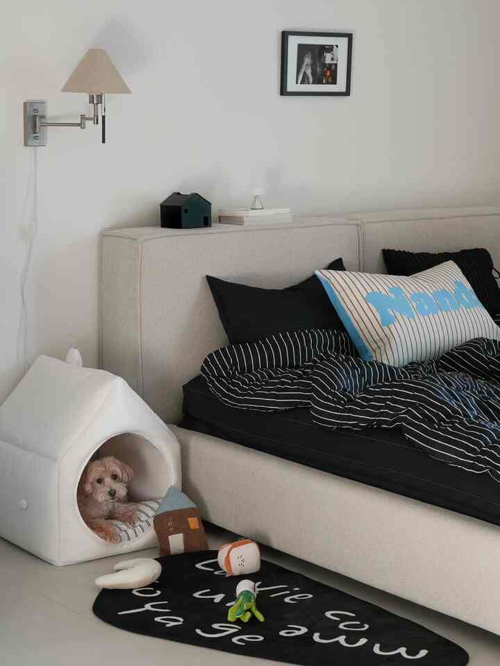 白とベージュの落ち着いた色調の寝室に、枕と黒いストライプの寝具を備えたベッドと犬用の白いペットハウスが配置された雰囲気のあるインテリア