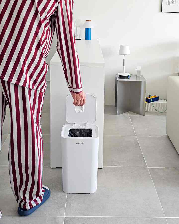 白とグレーの色調のリビング、中央に白いチェストとゴミ箱、右にソファとサイドテーブルが配置された清潔感のある空間