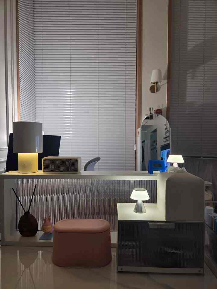 ピンクのミニスツールと白いデスク、ナイトテーブル、テーブルランプが配置されたモダンなホームオフィスの雰囲気あるインテリア