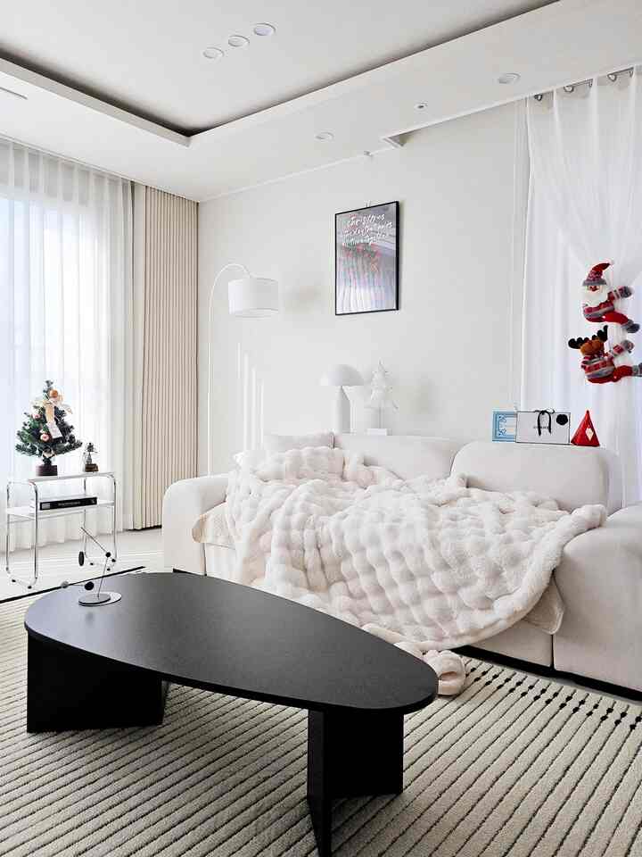 白とベージュのトーンのリビング、大きなソファと黒のコーヒーテーブルが配置された印象的な自然な空間