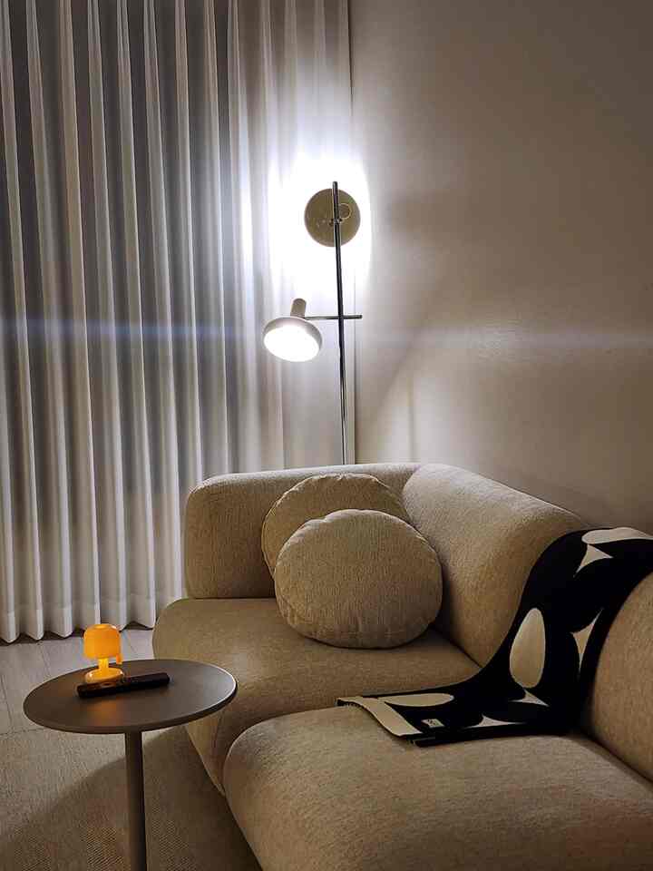 ベージュ色調のリビング、ミッドセンチュリーモダンスタイルのソファとフロアランプが配置された雰囲気のある空間