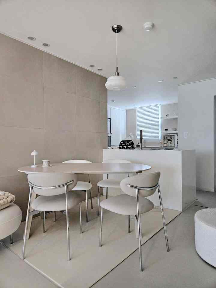 モダンなホワイトとベージュのキッチン空間、楕円形のポーセリンダイニングテーブルとシリコンレザーのチェアが配置された清潔感のあるインテリア