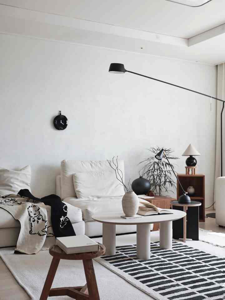 A white and black harmonious living room featuring a natural modern sofa, wooden stool, and floor lamp in a stylish setting