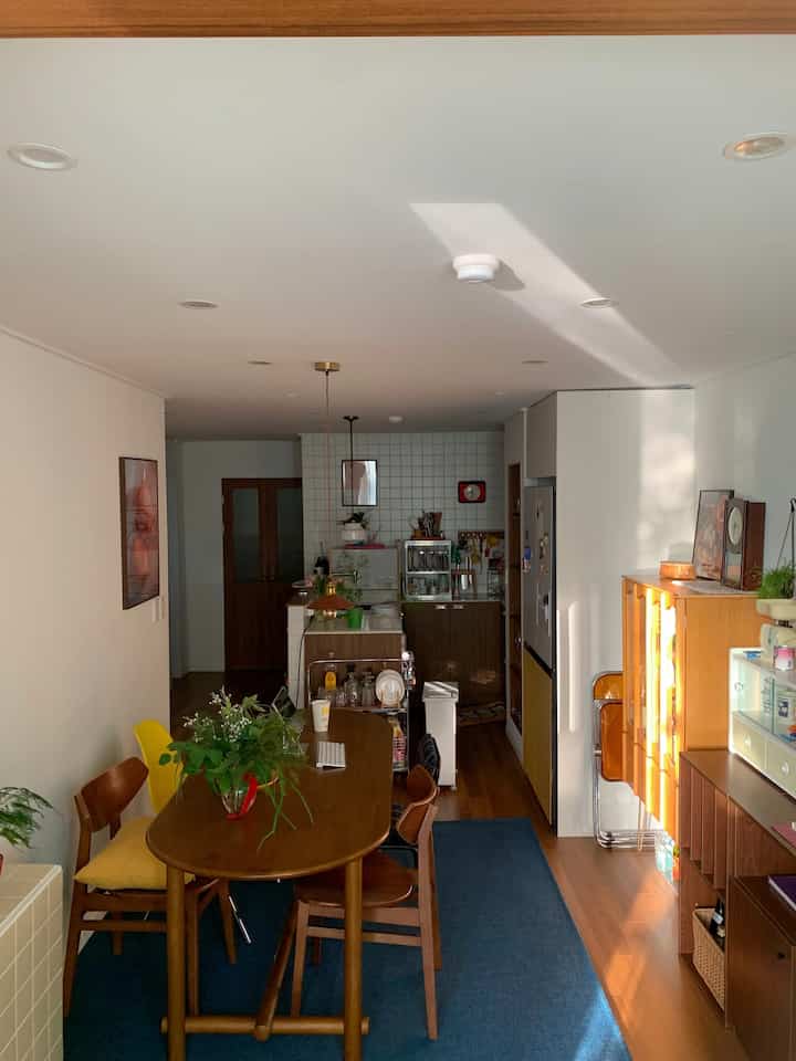 暖かい木目調とネイビーのラグが調和した狭い築古アパートのリビングとキッチンが融合した雰囲気のある空間