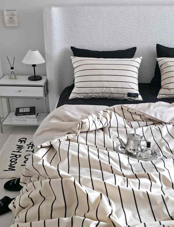 白と黒のトーンの寝室、ストライプの寝具と小さなテーブルランプが配置された、シンプルで清潔感のある印象的な空間