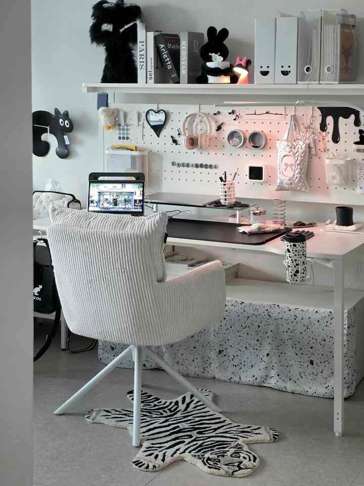 White and black toned studio home office featuring a soft corduroy chair, clean desk, and animal-patterned rug in a simple modern space