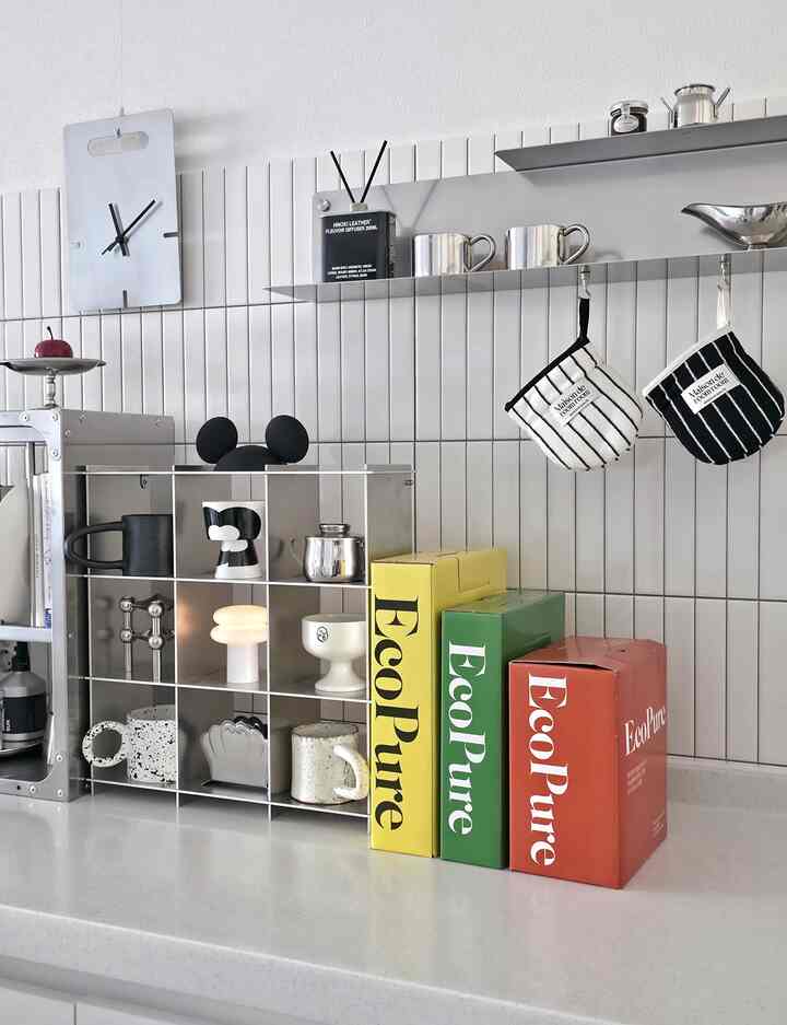 白い壁とシルバーのメタル棚に様々なキッチン用品とディフューザーが配置された清潔感のあるキッチンカウンターの空間