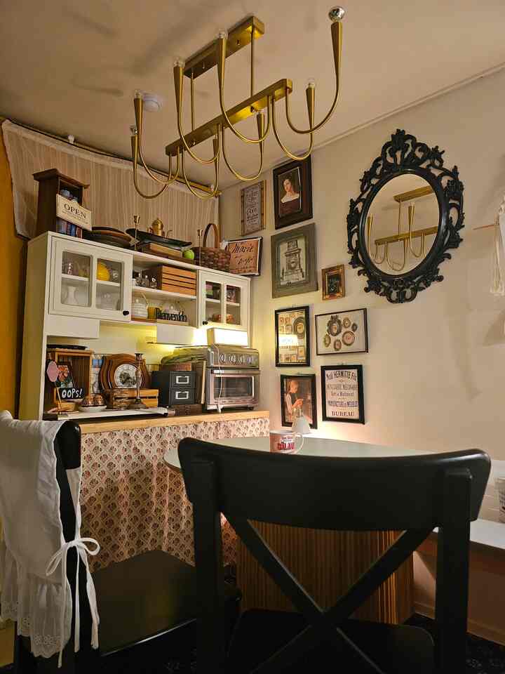 ホワイトとゴールドのトーンが特徴的なヴィンテージ風キッチン、壁飾りと照明が調和した印象的な小さな空間