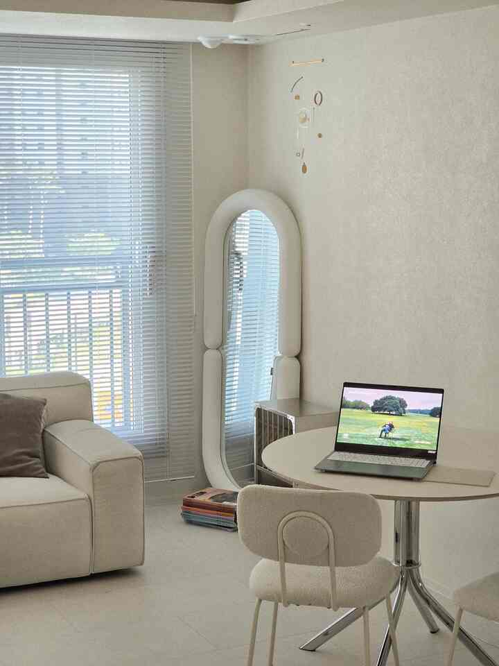 アイボリーとホワイト色調のダイニング兼リビングルーム、丸テーブルと全身鏡が配置されたシンプルでミニマルな雰囲気のインテリア