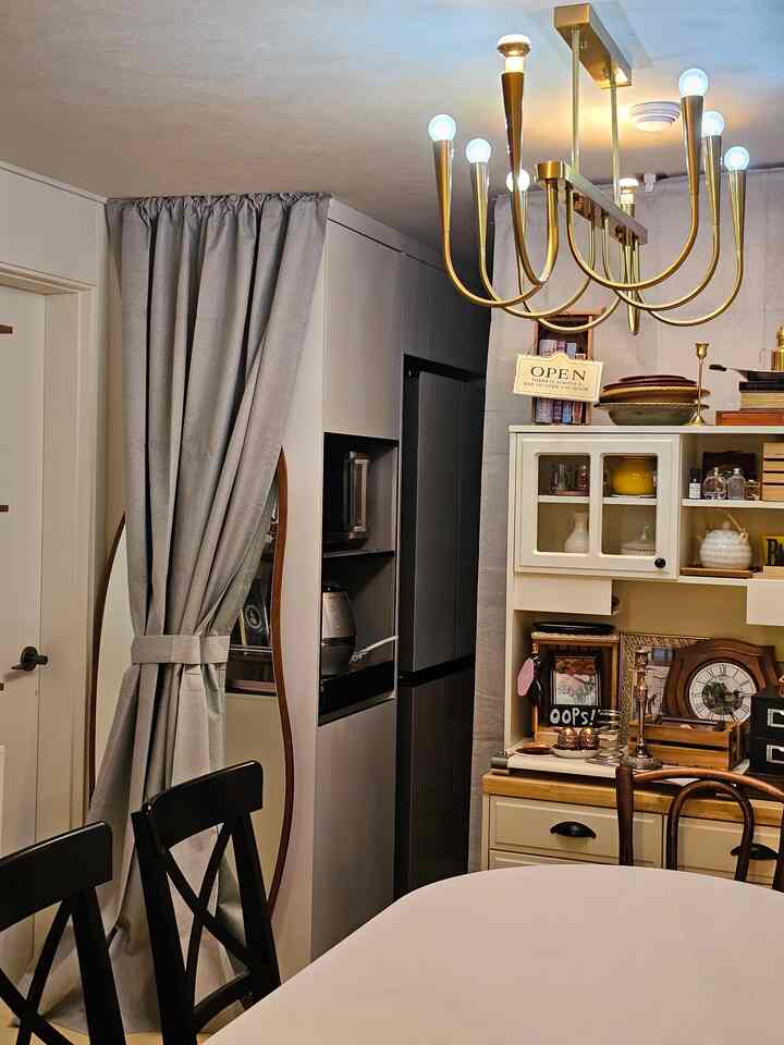 ゴールドの照明が印象的なキッチンとダイニング、ヴィンテージの小物と白いダイニングテーブルが配置された雰囲気のある空間