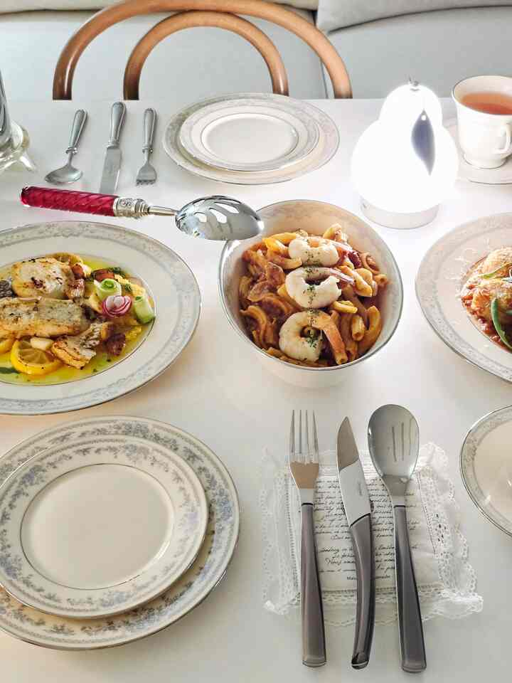 白を基調としたダイニングテーブルにヴィンテージのカトラリーセットと皿、エビのパスタが配置された雰囲気のあるおうちカフェインテリア